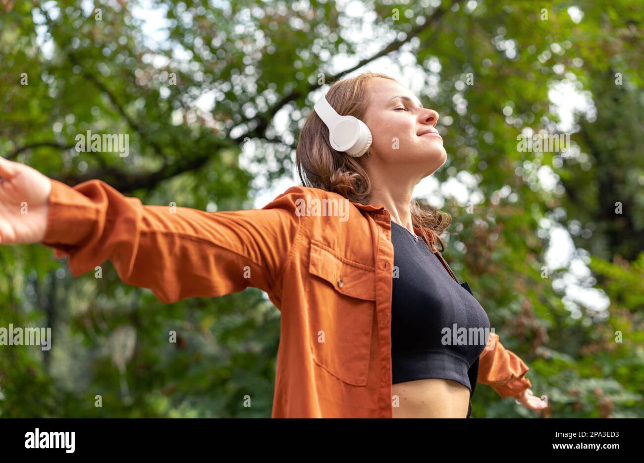 Eine Frau mit ausgestreckten Armen hört Musik in der Natur. Stockfoto