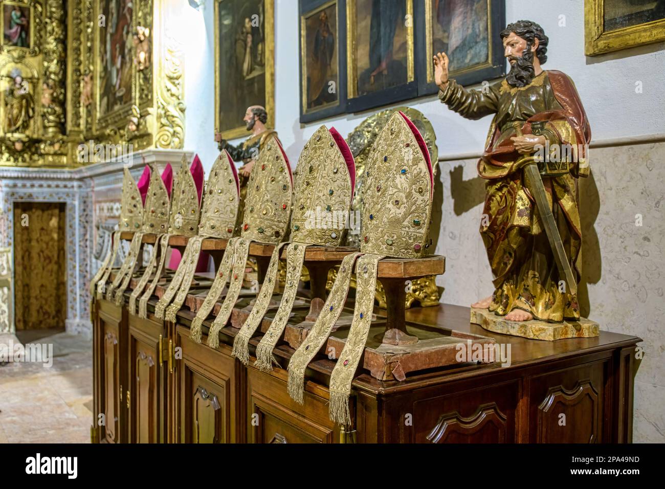 Kathedrale von Lissabon. Eine Gruppe von Birettas auf einem alten Möbelstück in einem berühmten katholischen Gebäude. Religiöse heilige Skulptur nebenan Stockfoto