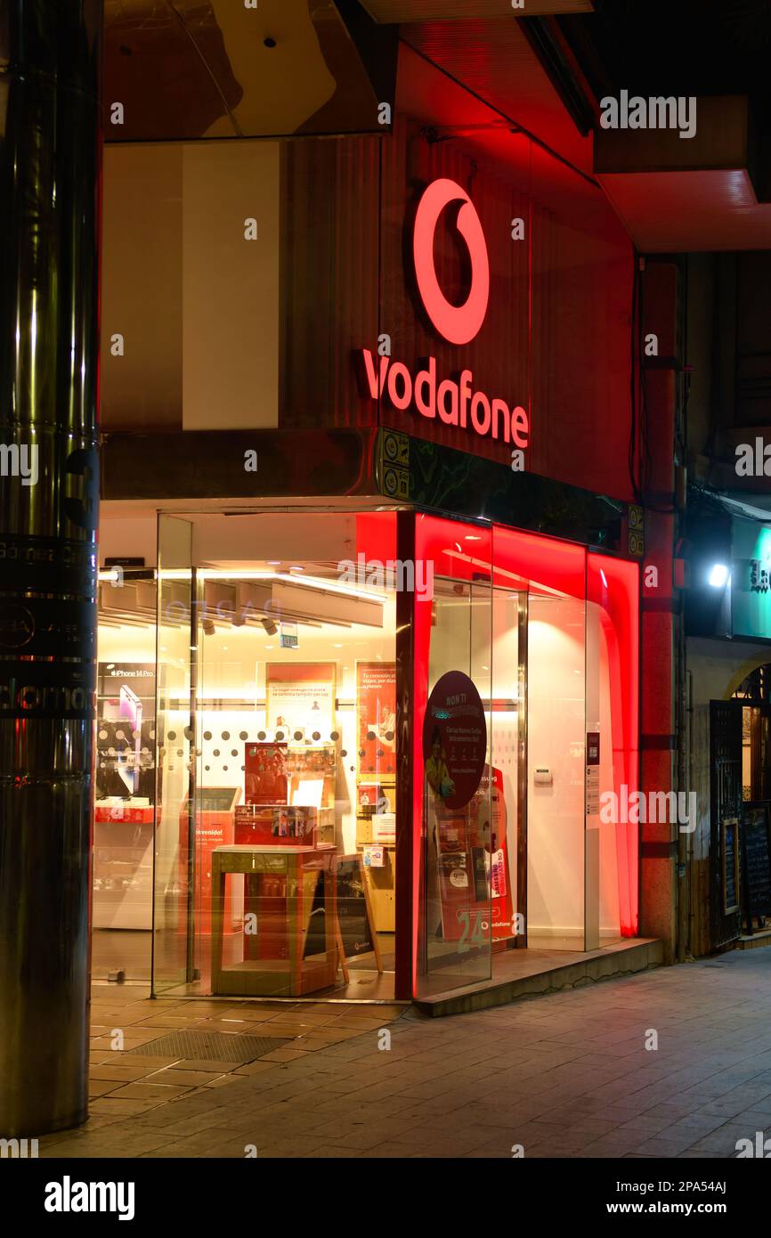Beleuchtetes Business-Schild oder Logo in einem Geschäft oder Geschäft in Vodafone. Szene der Stadt Alicante bei Nacht in Spanien. Stockfoto