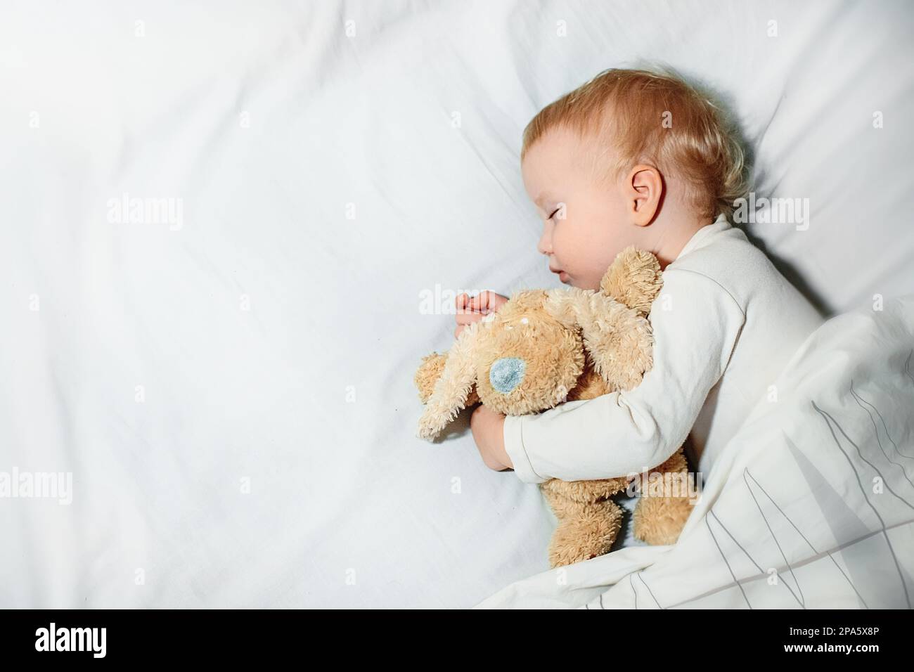 Süßes kleines Mädchen schläft auf weißer Bettwäsche im Bett. Das 1-jährige Kind schläft in der Umarmung des Spielzeugs. Glückliche Kindheit und Schlafprobleme bei Kindern Konzept Stockfoto