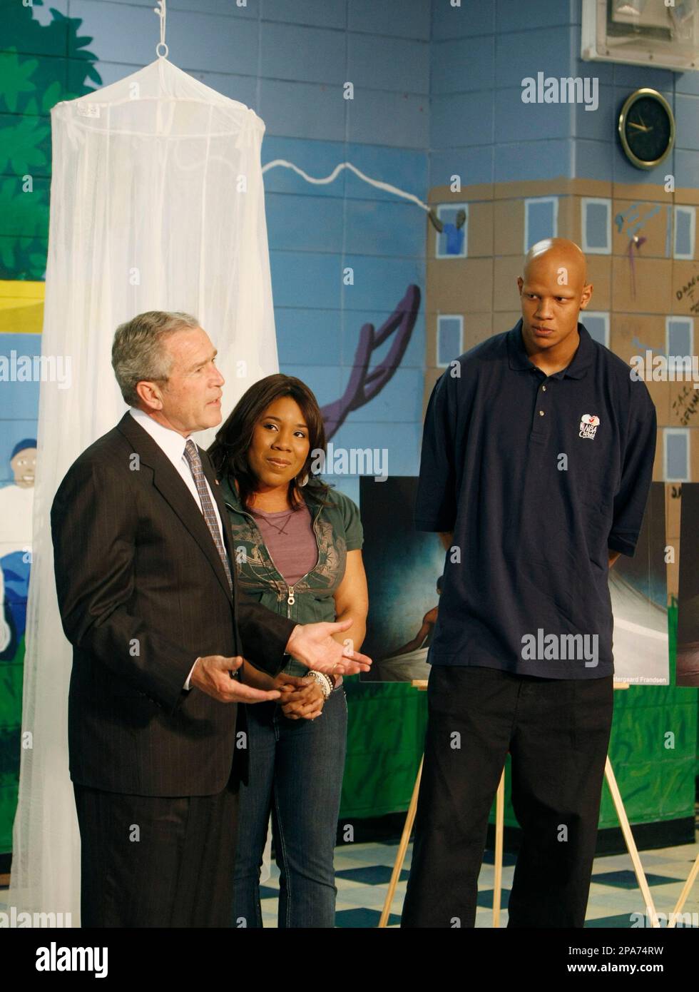 President Bush speaks about Malaria awareness in front of a mosquito net as he tours the Northwest Boys and Girls Club in Hartford, Conn., Friday, April 25, 2008. With him are former American Idol finalist Melinda Doolittle, center, and Milwaukee Bucks basketball player Charlie Villanueva, right. (AP Photo/Gerald Herbert) Stockfoto