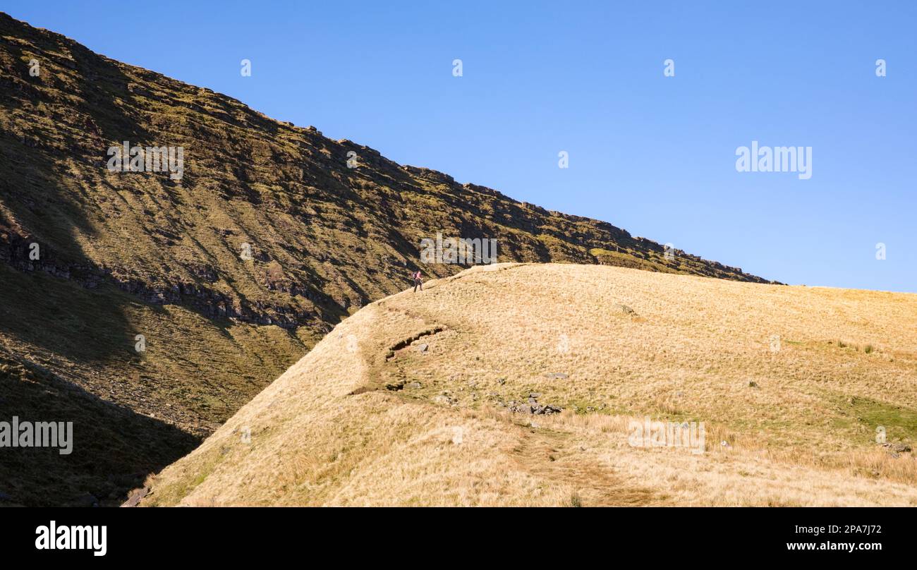 Walker führt den Weg nach Llyn y Fan Fawr unter den Old Red Sandsteinklippen von Fan Hir im Brecon Beacons National Park von South Wales UK hinauf Stockfoto