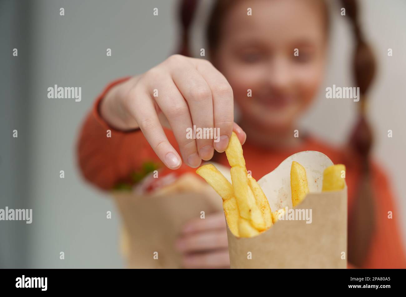 Ein kleines weißes Mädchen isst Pommes in einem Fast-Food-Restaurant. Nahaufnahme eines weiblichen Kindes, das Kartoffelstäbchen aus einer Schachtel nimmt Stockfoto