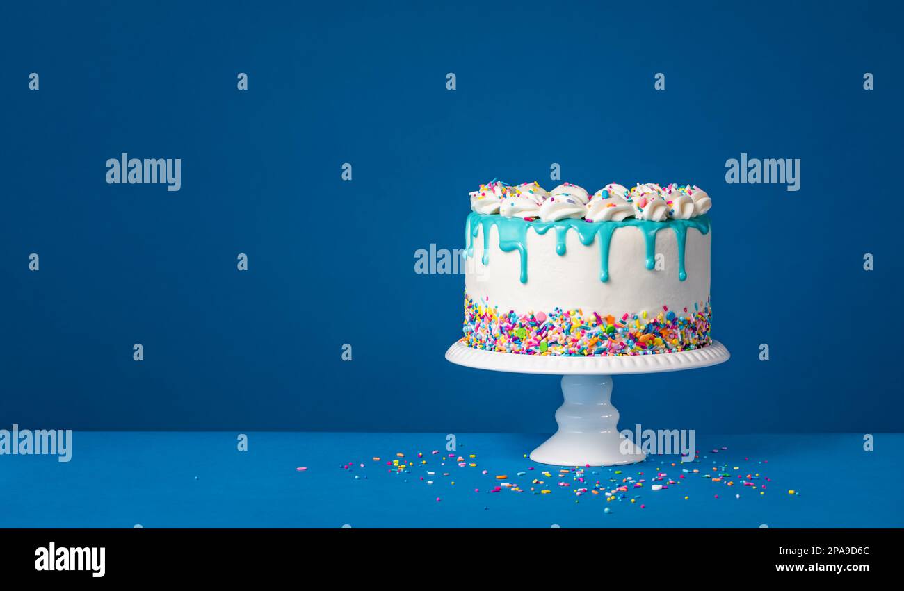 Weißer Geburtstagskuchen mit türkisgrüner Ganache und bunten Streuseln auf dunkelblauem Hintergrund. Einfach und trendig. Speicherplatz kopieren. Stockfoto