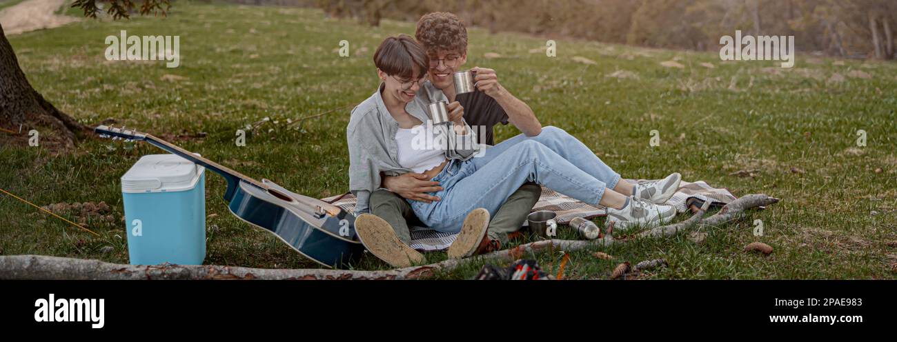 Fröhliche junge Touristen, die in Umarmung sitzen und beim Picknick lachen. Wochenende. Stockfoto
