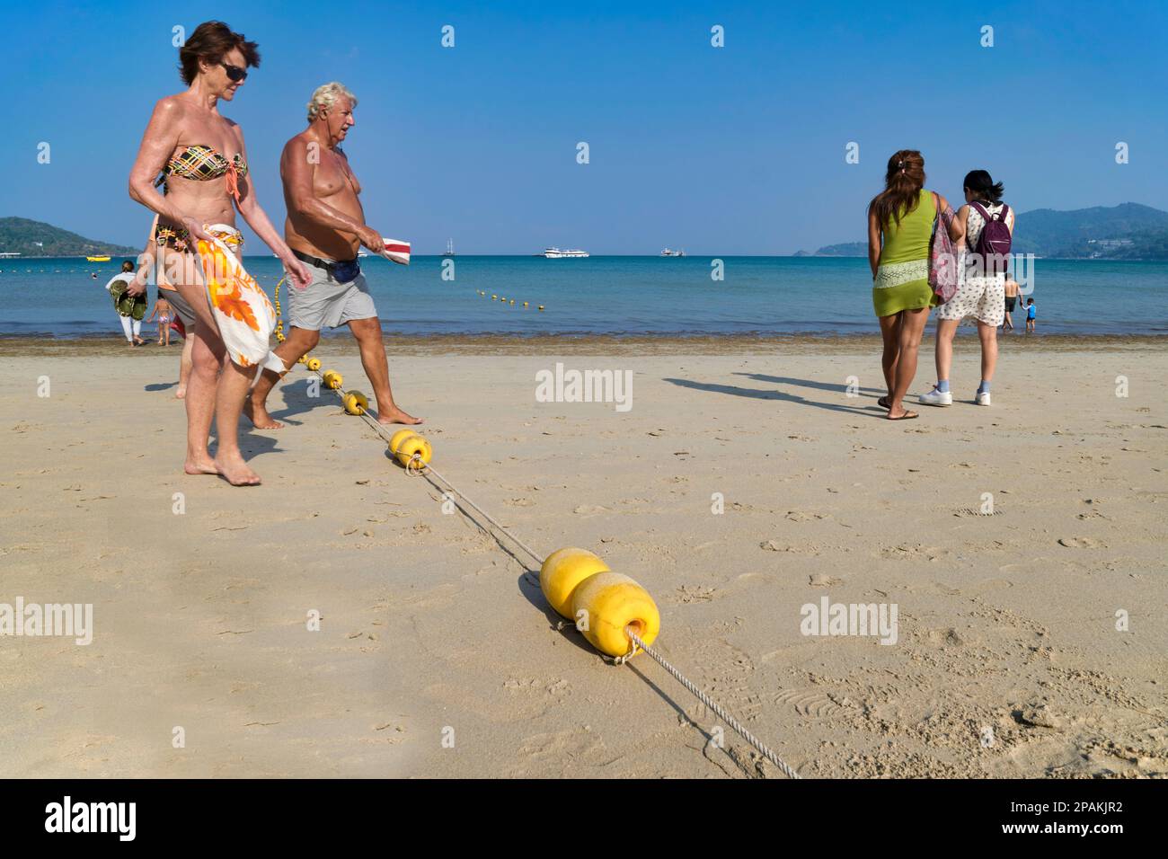 Ein Touristenpaar in Patong Beach, Phuket, Thailand, tritt über eine Reihe von Bojen, die die Bereiche zum Schwimmen und für motorisierten Wassersport abgrenzen Stockfoto