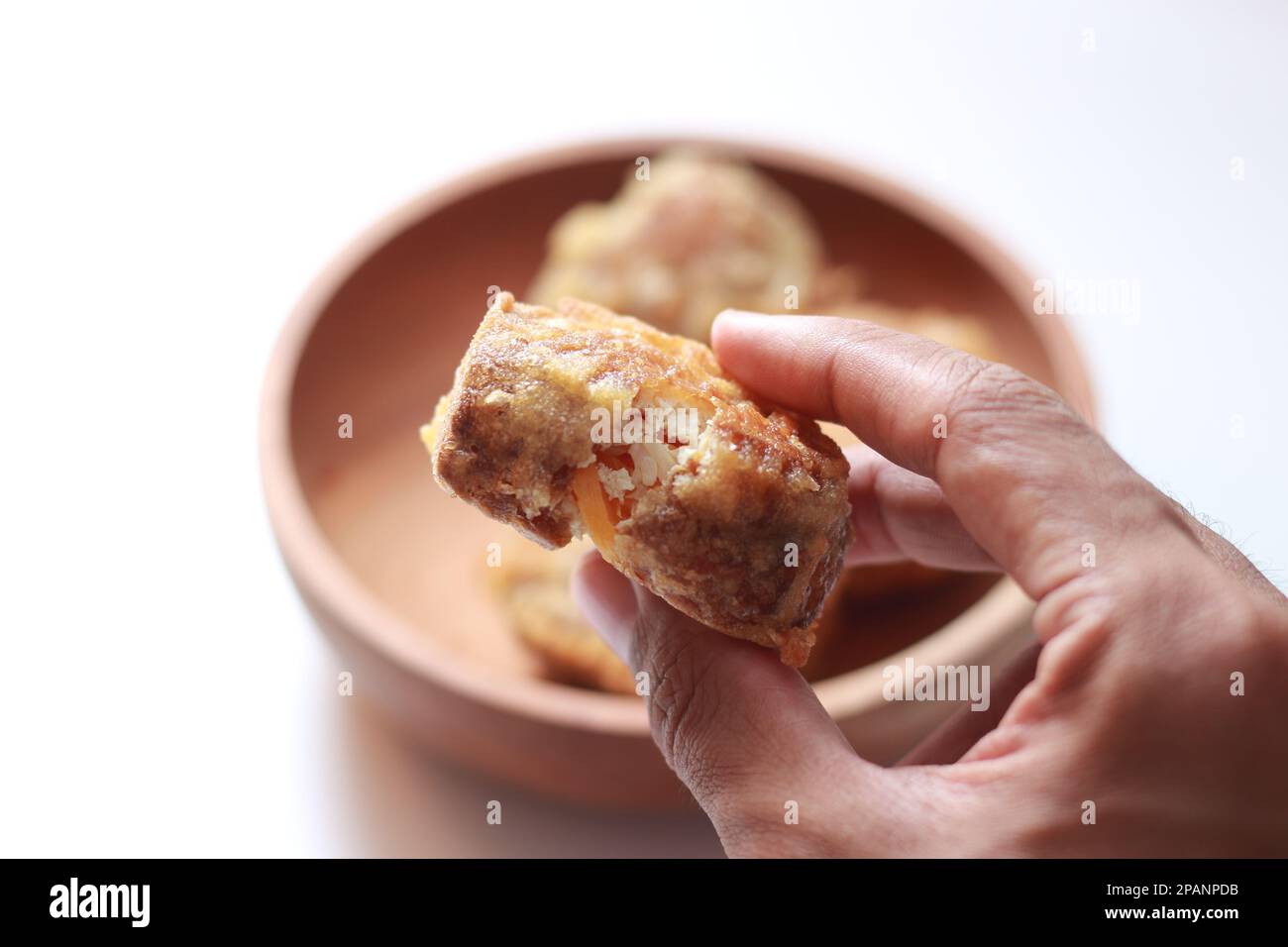 Nahaufnahme von gebratenem, gefülltem Tofu oder Gorengan Tahu ISI in der Hand isoliert auf weißem Hintergrund und Schüssel mit gefülltem, frittiertem Tofu verschwommen. Indonesisch f Stockfoto