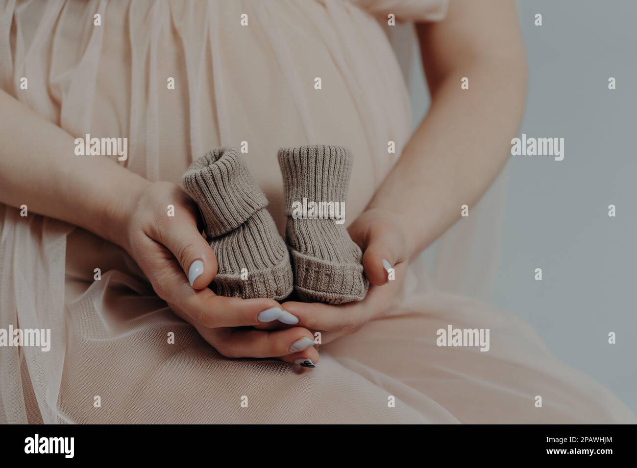 Mutterschafts- und Schwangerschaftskonzept. Werdende Mutter bereitet sich auf die Geburt des Kindes vor hält Stiefel in den Händen und stellt sich im dritten Trimester drinnen auf Stockfoto