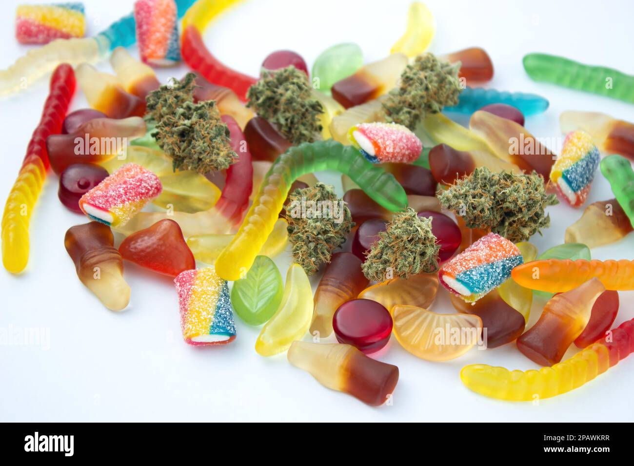 Getrocknete medizinische Marihuana-Knospen liegen zwischen Gummien verschiedener Formen und Geschmacksrichtungen. Auf einem kaltweißen Hintergrund Stockfoto