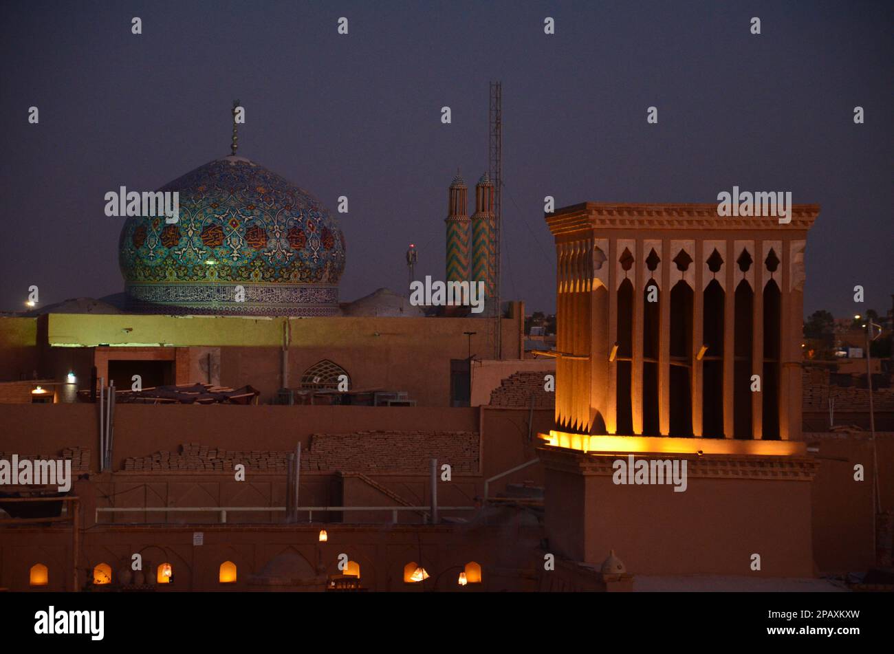 Beleuchteter Windturm und farbenfrohe Kuppel einer Moschee in Yazd, Iran im Abendlicht Stockfoto