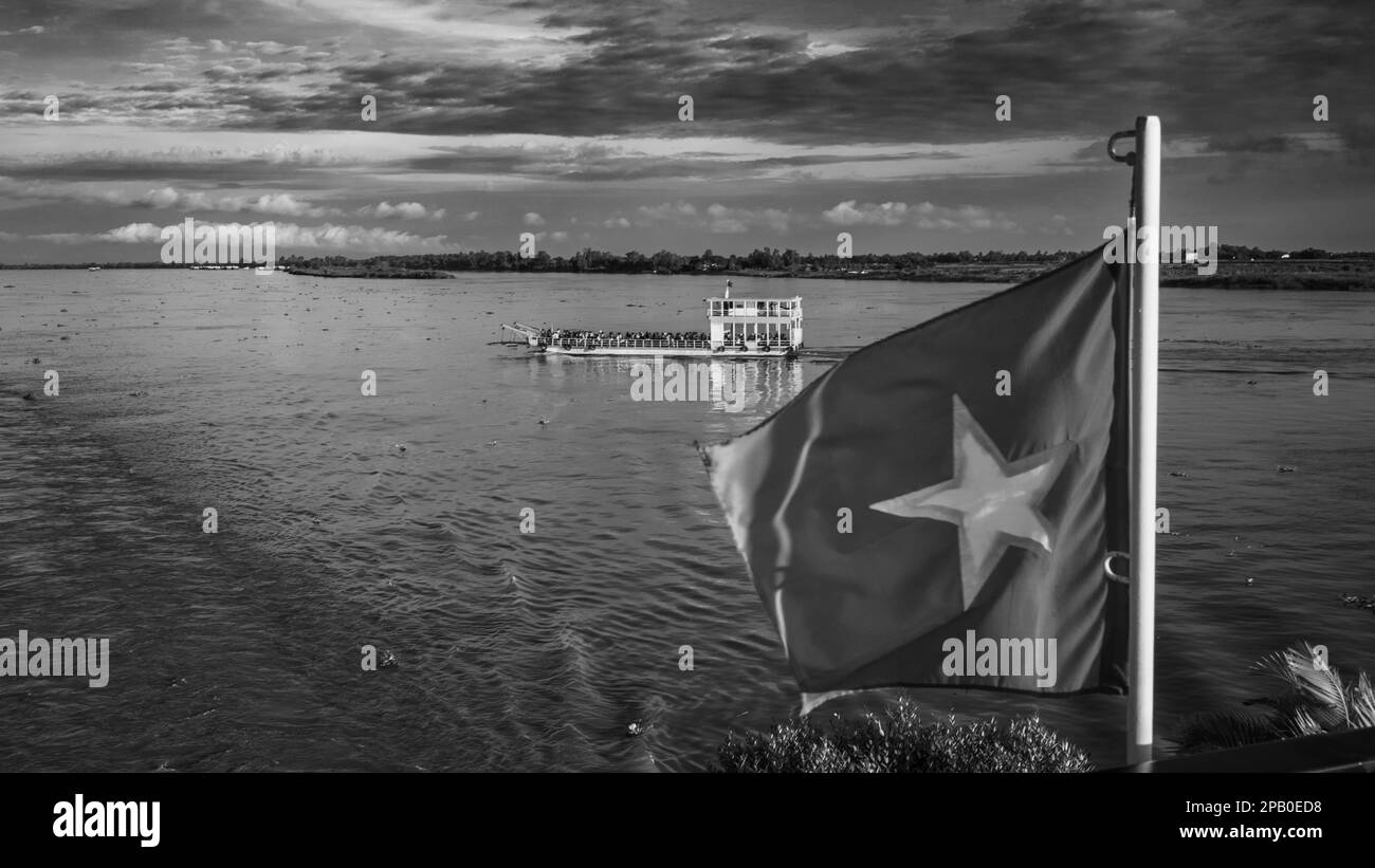 Eine überfüllte Flussfähre überquert den Mekong, vorbei an einer vietnamesischen Flagge auf dem Heck des Flussschiffes Victoria Mekong kurz nach der Dämmerung Stockfoto