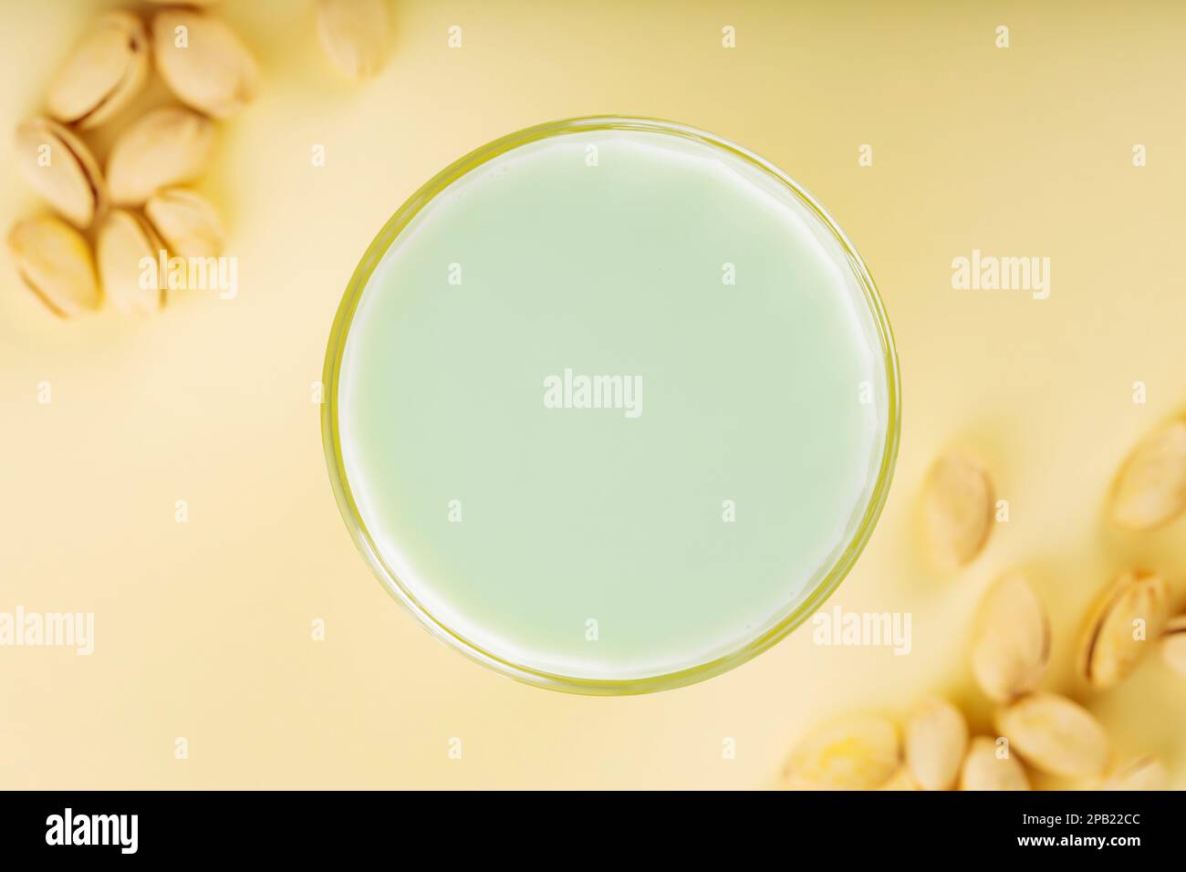 Pistazienmilch in Glas und getrocknete Pistazien auf pastellgelbem Hintergrund. Lactosefreie Pistazienmilch für die diätetische Ernährung. Draufsicht Stockfoto