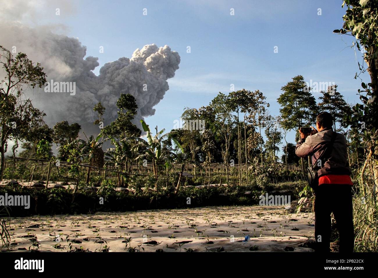 Boyolali, Indonesien. 12. März 2023. Ein Mann macht Fotos, während vulkanische Materialien vom Vulkan Mount Merapi in Boyolali, Zentraljava, Indonesien, gespuckt werden, 12. März 2023. Indonesiens Vulkan Mount Merapi brach am Samstag aus und spuckte vulkanische Asche in mehrere nahe gelegene Dörfer, berichtet das Forschungs- und Entwicklungszentrum für Geologische Katastrophen (BPPTKG) des Landes. Kredit: Bram Selo/Xinhua/Alamy Live News Stockfoto