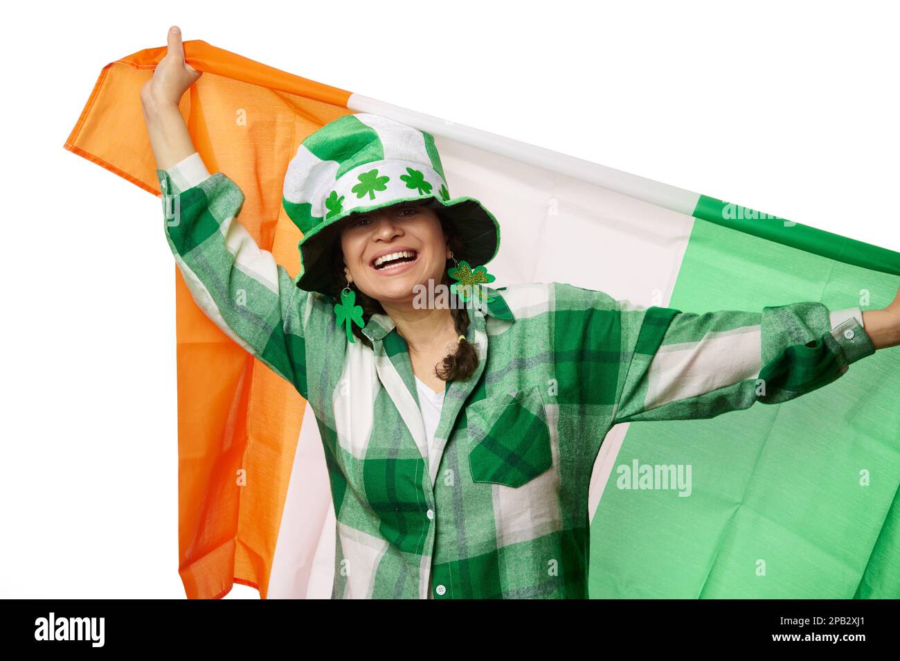 Hübsche Frau mit St. Patricks Hut und Klee hinterlässt Ohrringe, lächelnd, mit der Flagge Irlands. Irische Kulturtraditionen Stockfoto