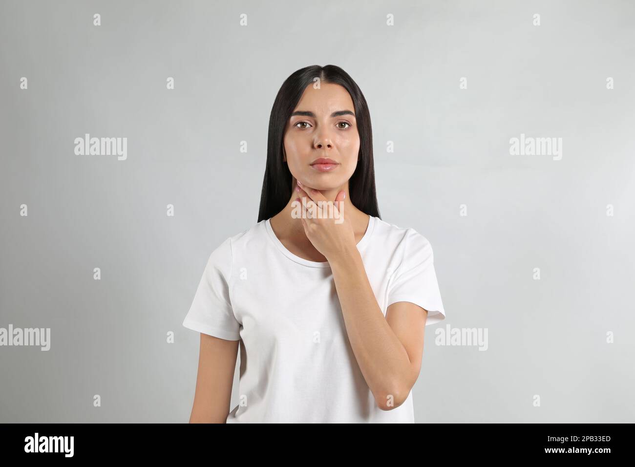 Junge Frau, die Schilddrüsen-Selbstuntersuchung vor hellem Hintergrund durchführt Stockfoto