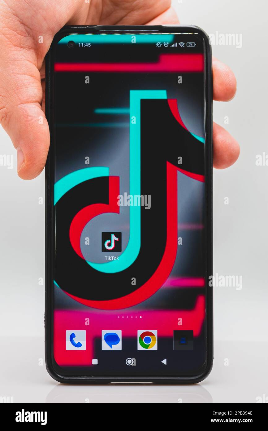 Ein Mann hält ein Smartphone mit TikTok-Hintergrundbild und TikTok-Anwendungssymbol auf dem Mobiltelefonbildschirm Stockfoto