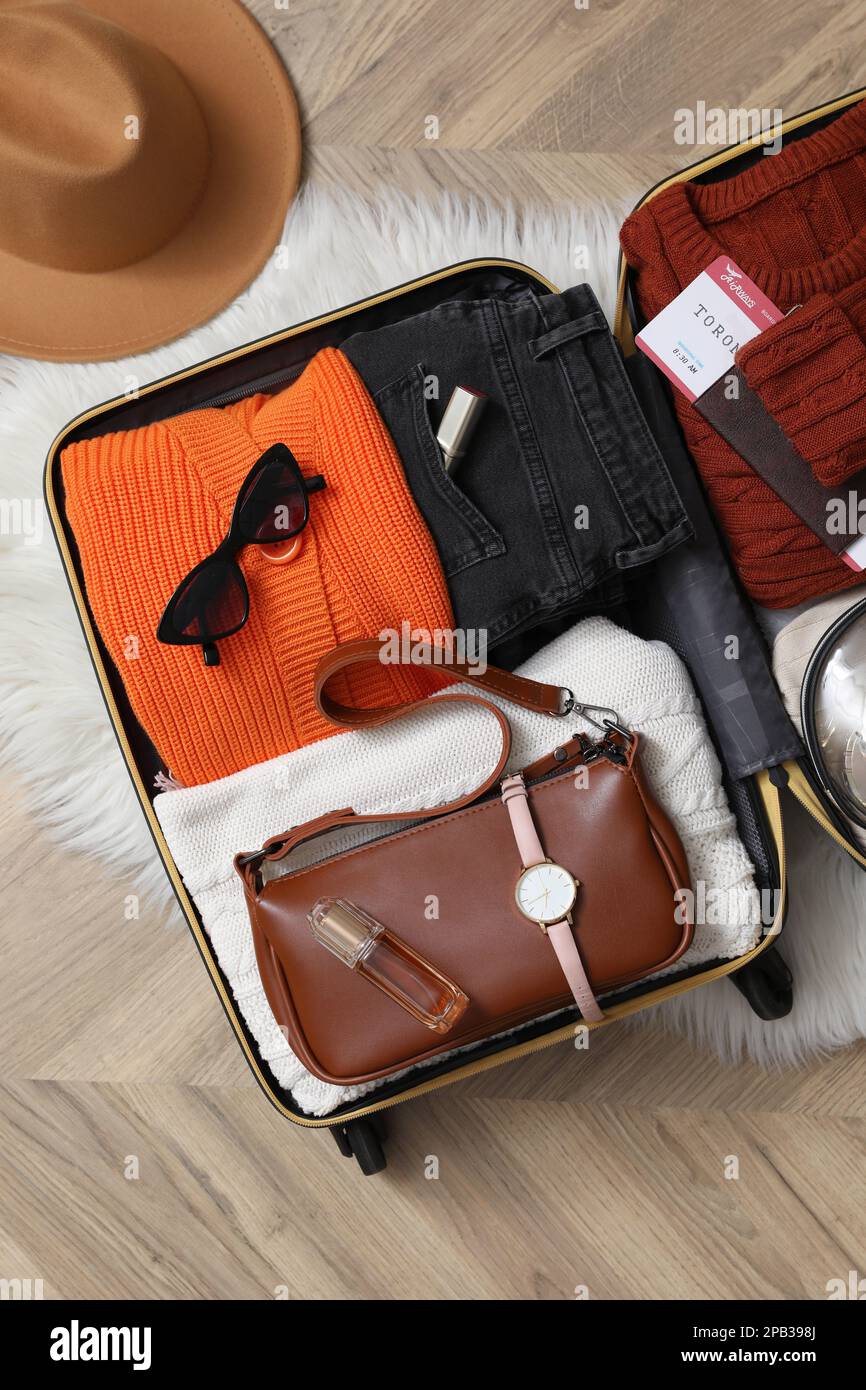 Offener Koffer mit gefalteter Kleidung und Accessoires auf dem Boden, flach liegend Stockfoto