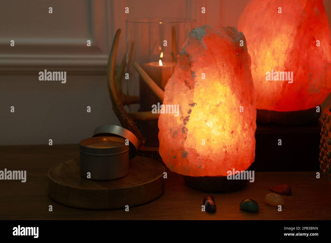 Salzlampen, Kerzen und Edelsteine des Himalaya auf einem Holztisch in der Nähe weißer Innenwände Stockfoto