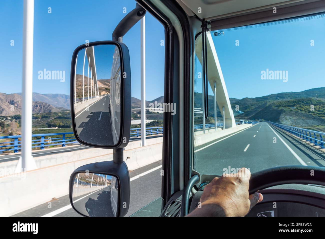 Sicht vom Fahrstand eines Lkws auf die Straße, auf der er beim Überqueren einer Brücke fährt, und auf die Rückspiegel. Stockfoto