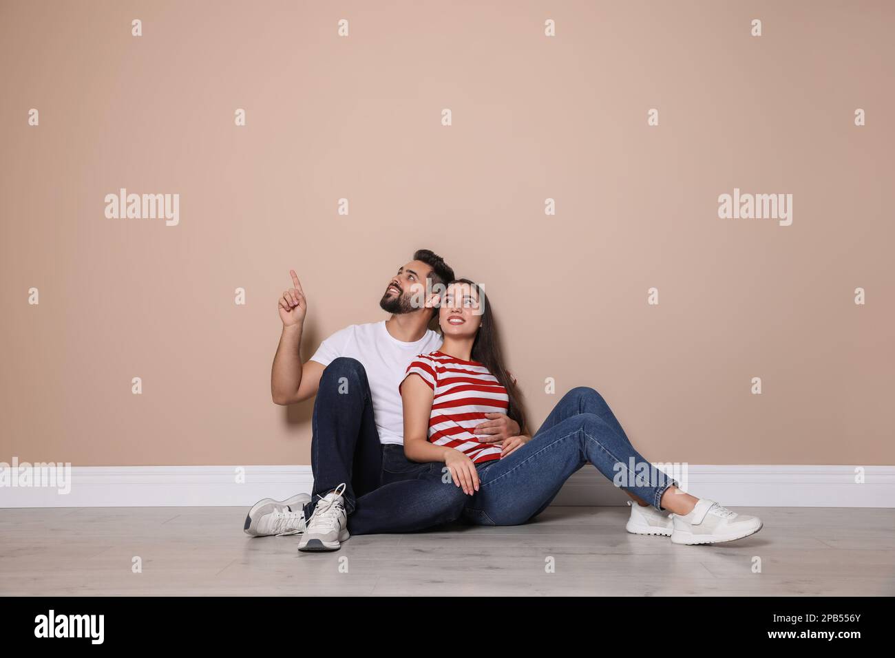 Ein junges Paar, das auf dem Boden neben beigefarbenen Wänden im Haus sitzt Stockfoto