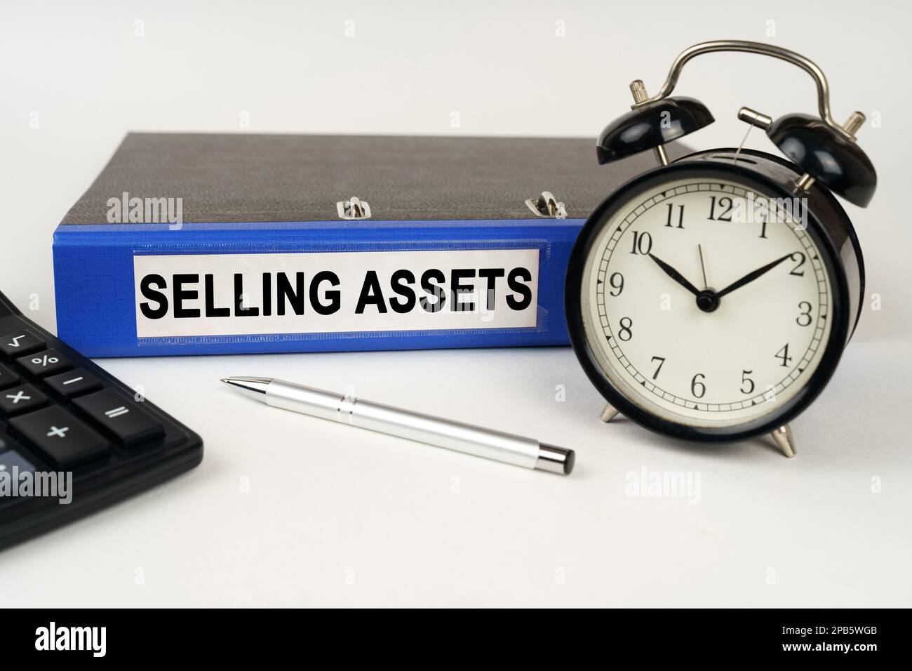 Geschäftskonzept. Auf einer weißen Oberfläche, einem Weckrechner und einem Ordner mit der Aufschrift „Selling Assets“ Stockfoto