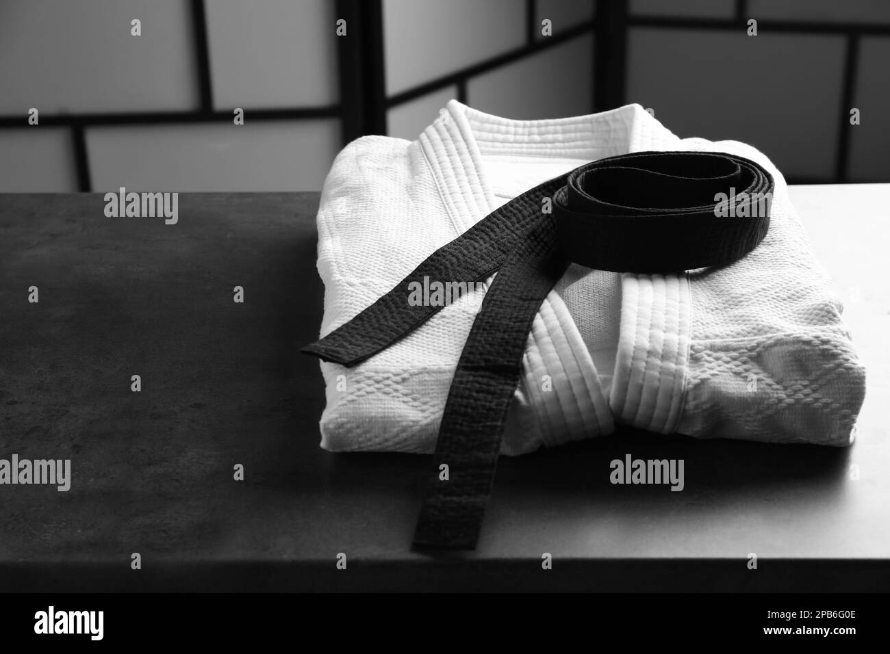 Kampfsport-Uniform mit schwarzem Gürtel auf grauem Steintisch drinnen Stockfoto