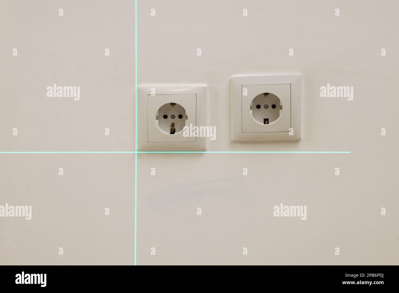 Verwendung von Kreuzlinien-Laser-Nivelliergeräten für die genaue Installation der Steckdose in der weißen Wand Stockfoto