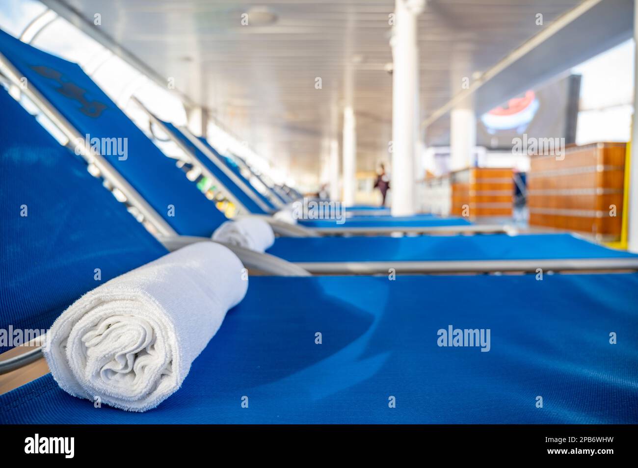 Ein gerolltes Handtuch auf einem Liegestuhl in einer Reihe auf einem Kreuzfahrtschiff Deck. Stockfoto