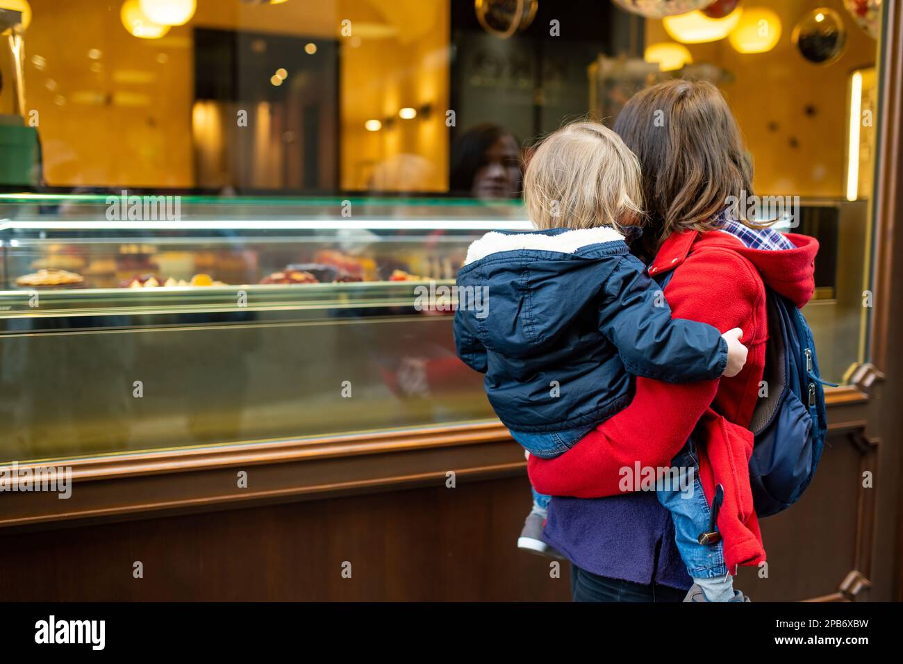 Junge Mutter hielt ihren kleinen Sohn fest, während sie auf die Bäckerei in der mittelalterlichen Straße der Stadt Bergamo nordöstlich von Mailand schaute. Malerische Aussicht auf Citta Alta, Stockfoto