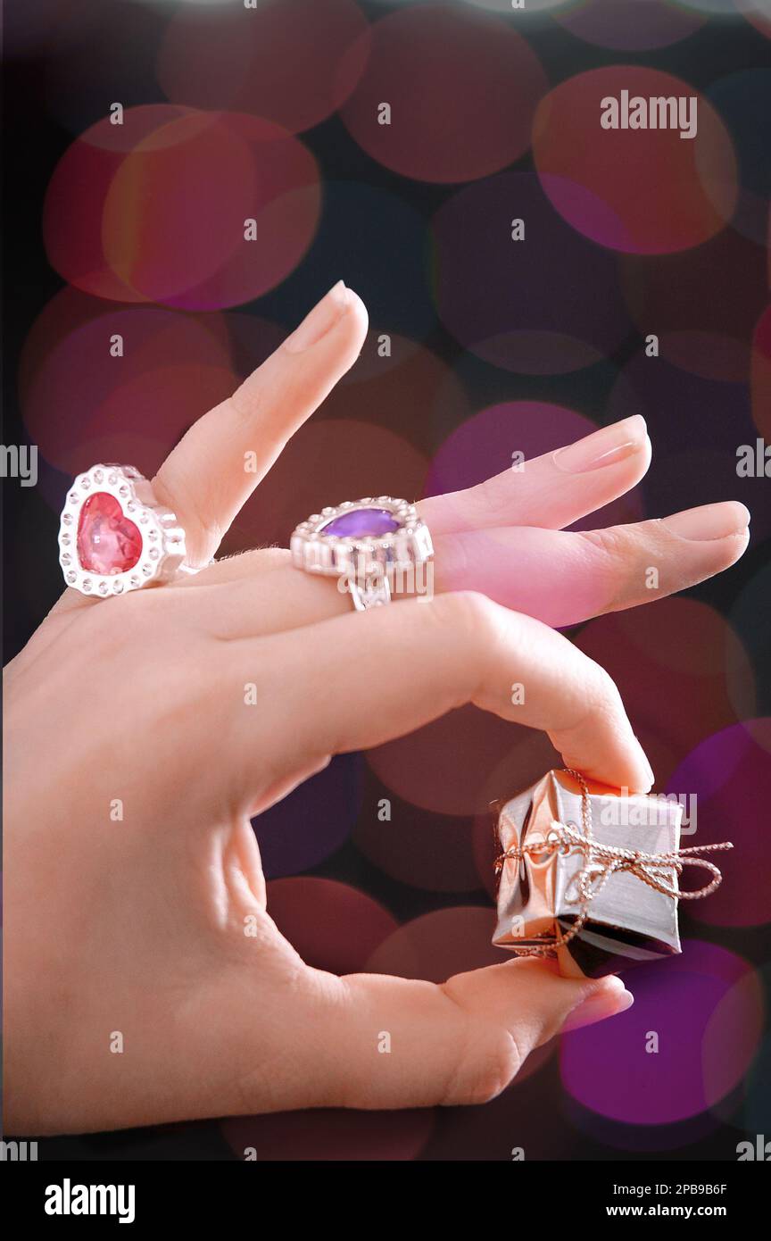 Die Hand einer Frau, die Ringe trägt und ein kleines Geschenk in der Hand hat Stockfoto