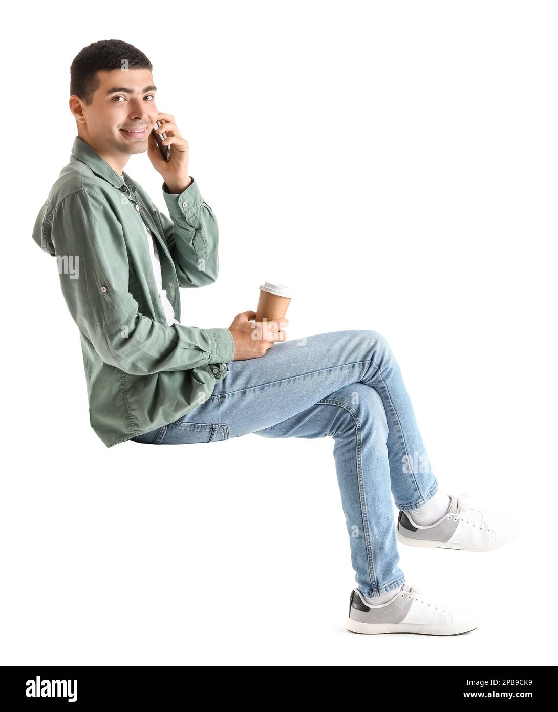Ein junger Mann mit einer Tasse Kaffee, der mit einem Handy im Stuhl auf weißem Hintergrund spricht Stockfoto