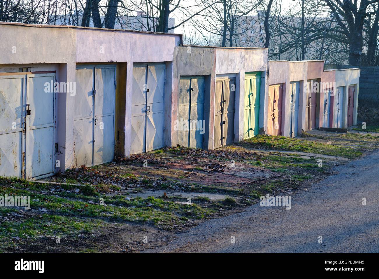 Betongaragen mit bunten Metalltüren im Morgensonnenlicht entlang einer Straße durch eine Baumgasse Stockfoto