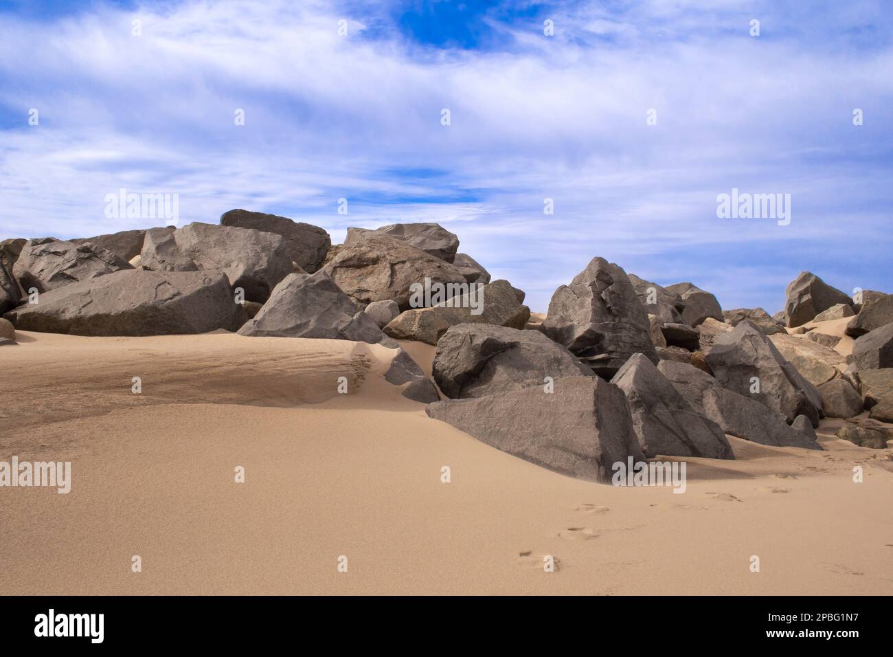 Sandstrand mit Felsen, Felsen. Blauer Himmel, weiche Wolken an einem Wintertag, Sandy Hook Beach, New Jersey, Teil der Gateway National Recreation Area. Stockfoto