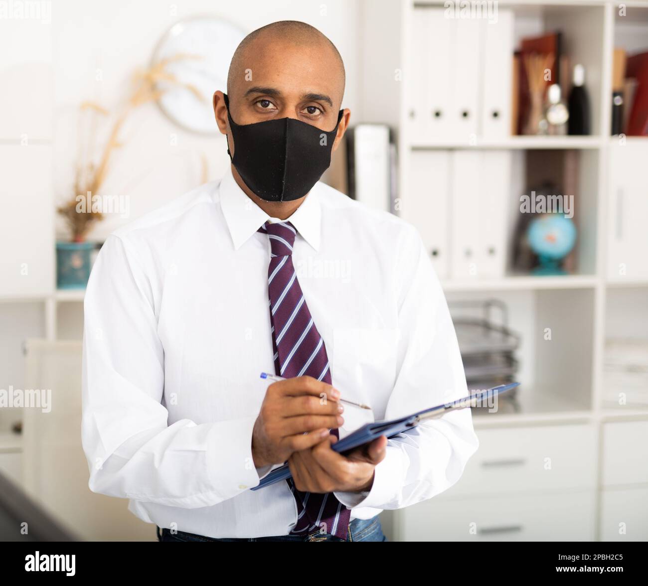 Geschäftsmann in Schutzmaske macht Notizen in Dokument Stockfoto