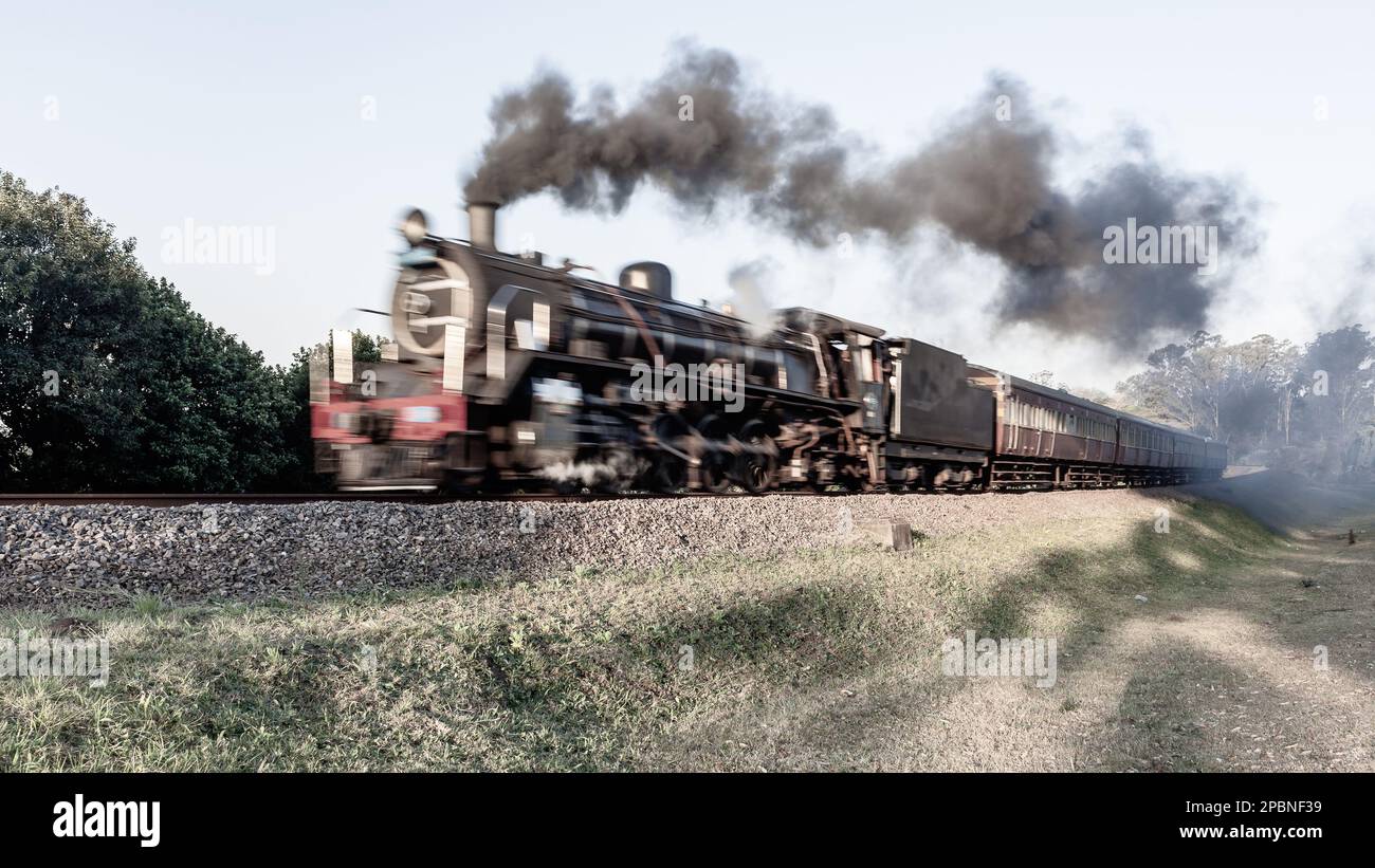 Dampflokomotive mit Touristenbussen schließt Bewegungsunschärfe auf Bahngleisen auf Landstraßen ab. Stockfoto