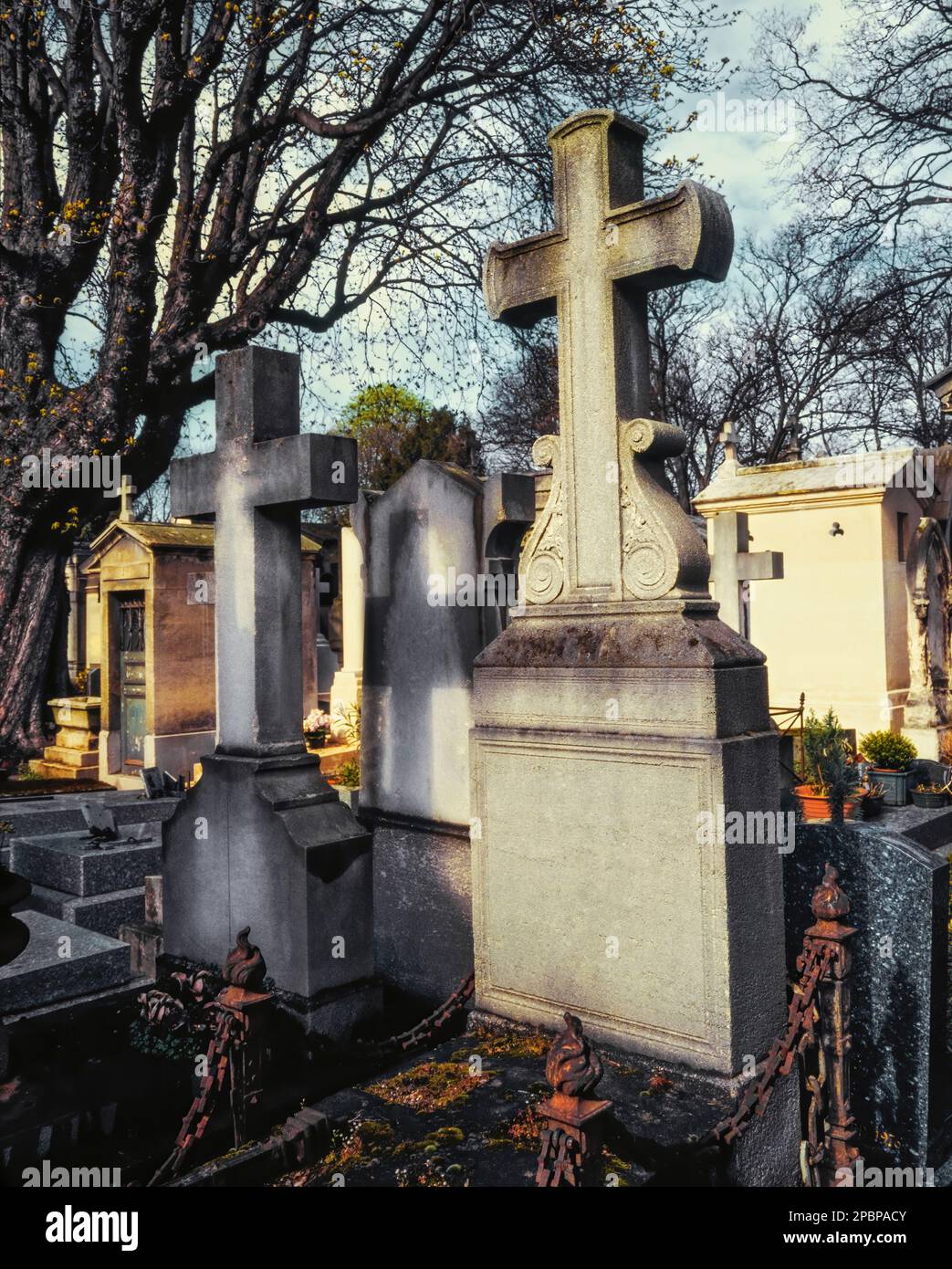 Verwitterte Steinkreuze und Gräber stehen feierlich in einem stillen Friedhof unter sanftem, gesprenkeltem Licht Stockfoto