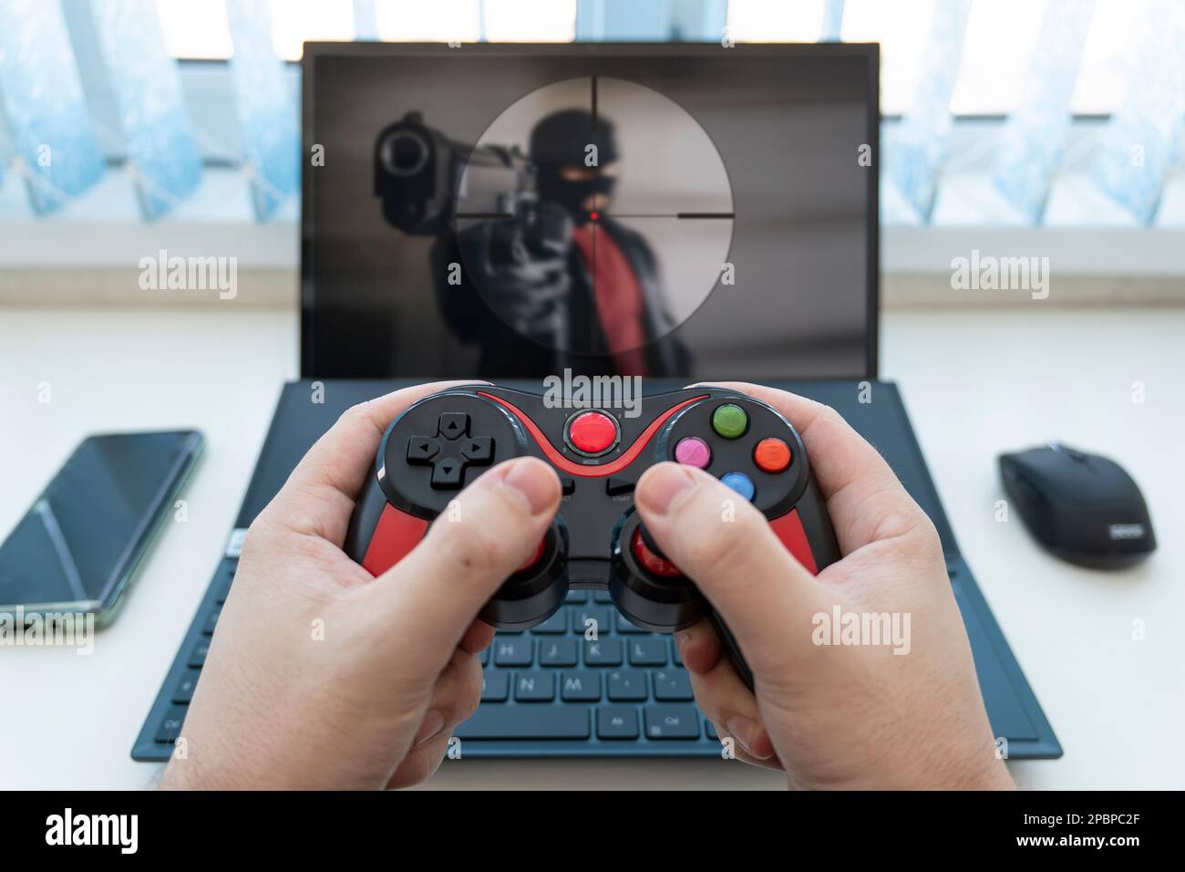 Der Joystick von der Spielkonsole ist schwarz und rot und der Laptop. Das Konzept der Spielebranche und ein lustiger Zeitvertreib zu Hause. Stockfoto