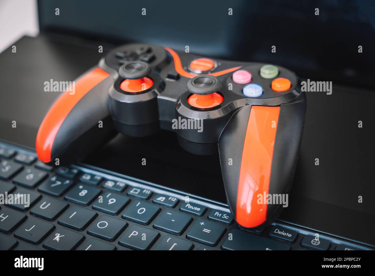 Der Joystick von der Spielkonsole ist schwarz und rot und der Laptop. Das Konzept der Spielebranche und ein lustiger Zeitvertreib zu Hause. Stockfoto