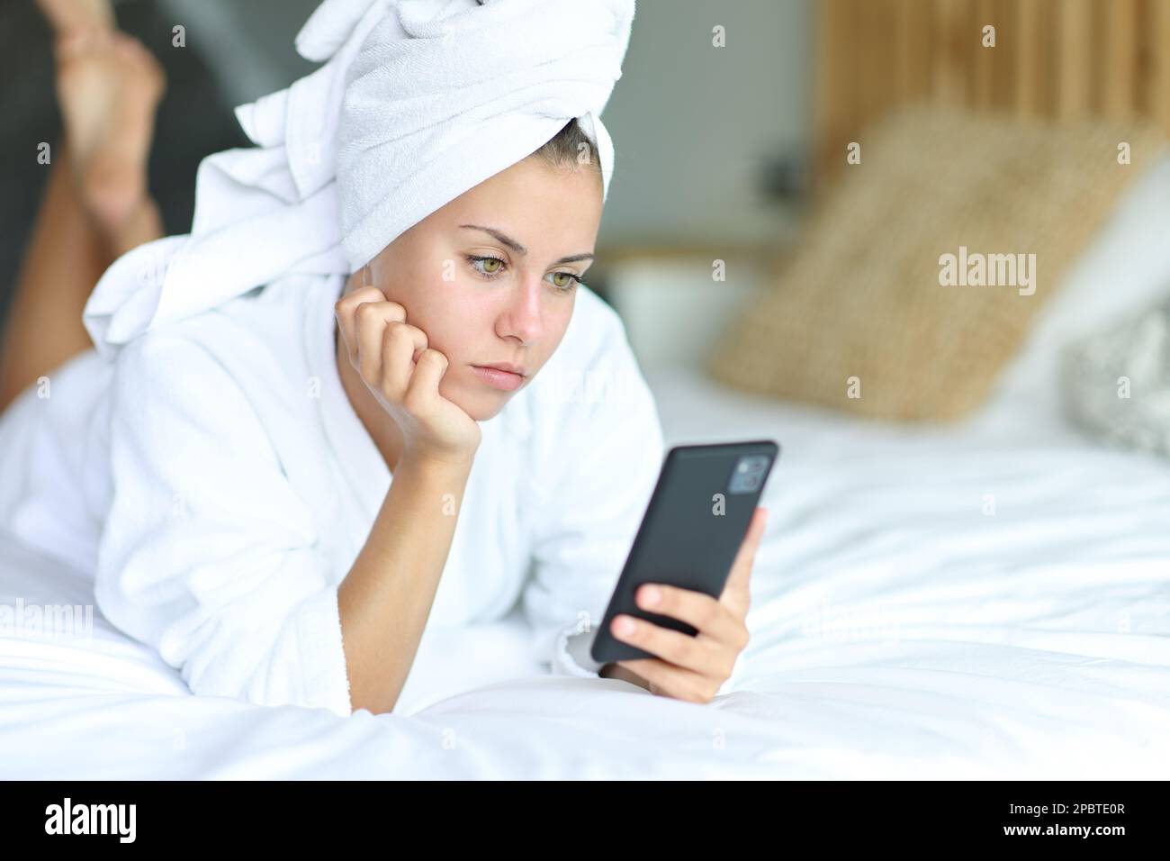 Ein ernster Teenager nach dem Duschen mit dem Handy auf dem Bett Stockfoto