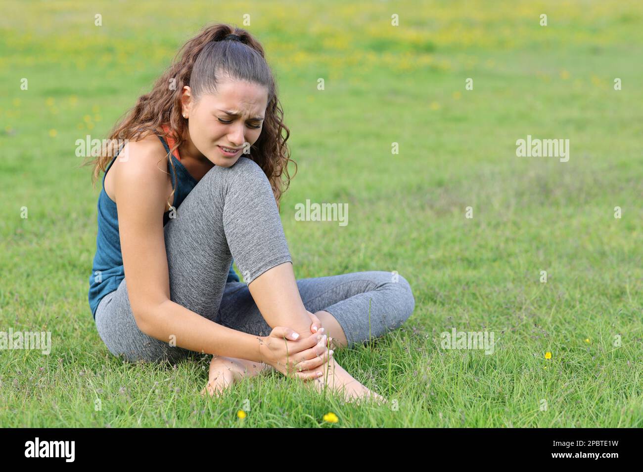 Yogi leidet an Knöchelschmerzen, sitzt auf dem Gras-Sportunfall Stockfoto