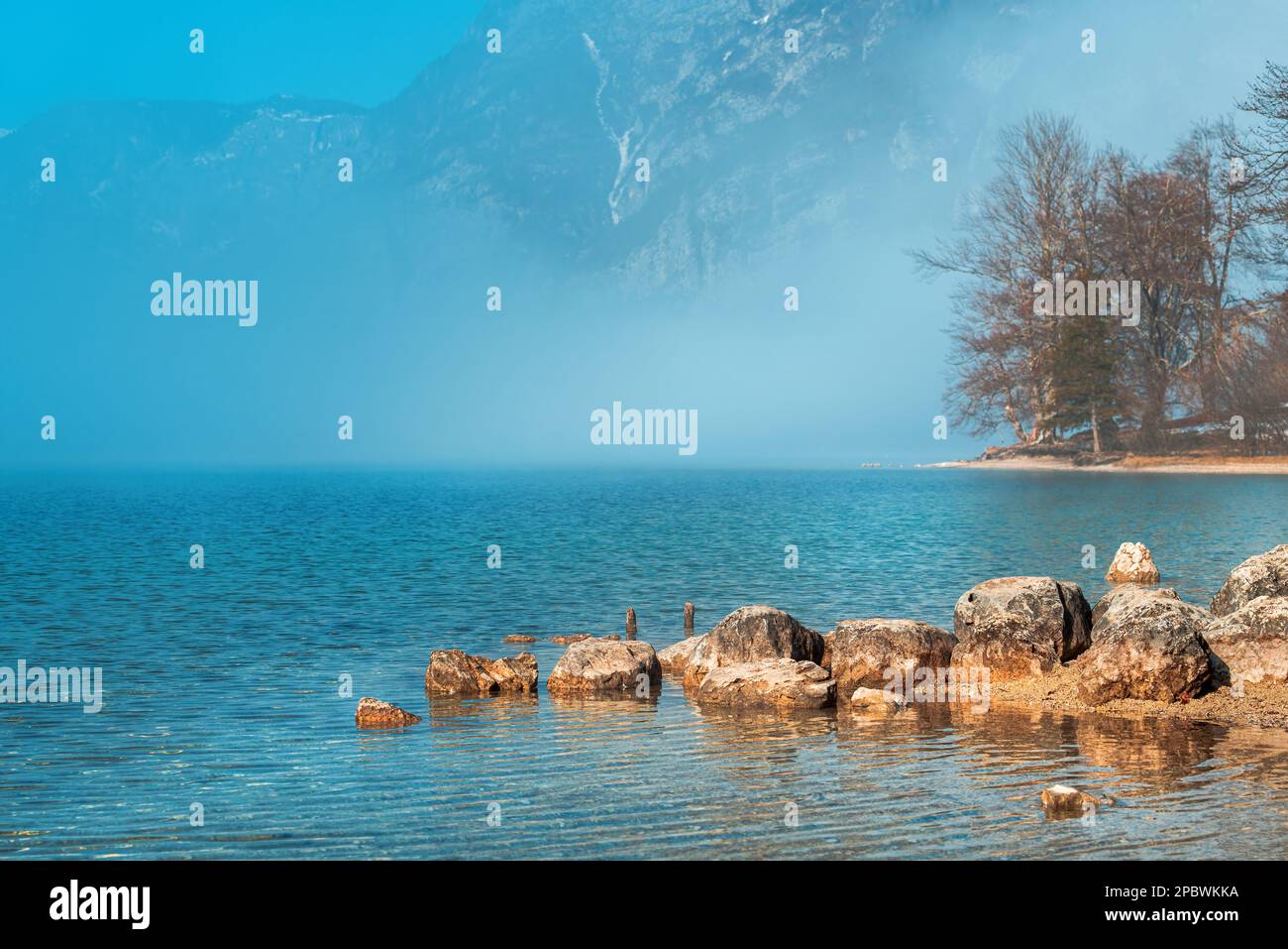 Große Felsen am Bohinjer Ufer mit Morgennebel über der Wasseroberfläche und Julischen Alpen im Hintergrund, selektiver Fokus Stockfoto