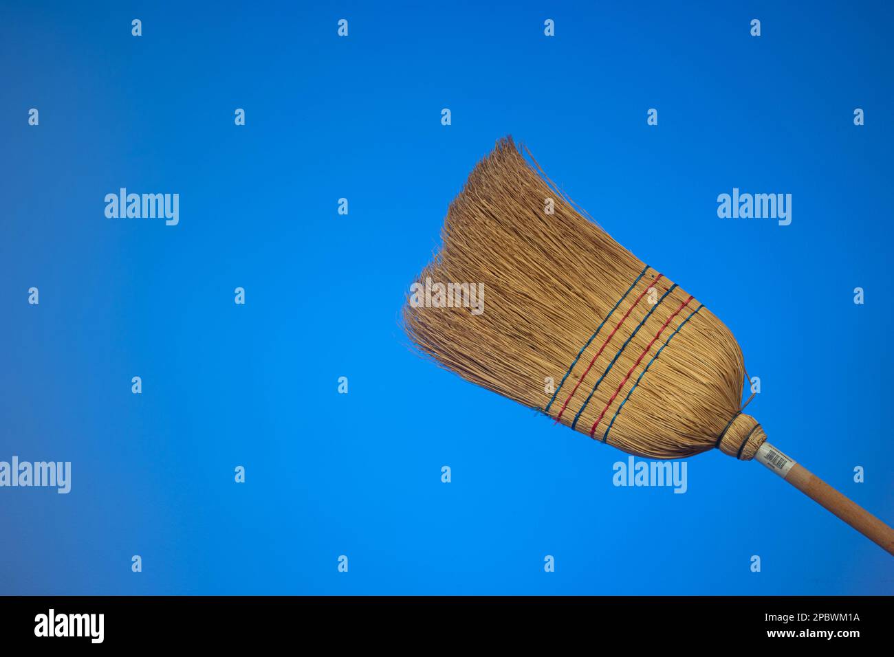 Strohbesen mit Holzgriff. Nahaufnahme des Studios, isoliert auf blauem Hintergrund. Stockfoto