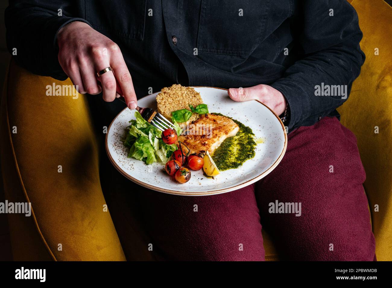 Ein Mann isst gegrillten Fisch mit Beilagen und Gemüse Stockfoto