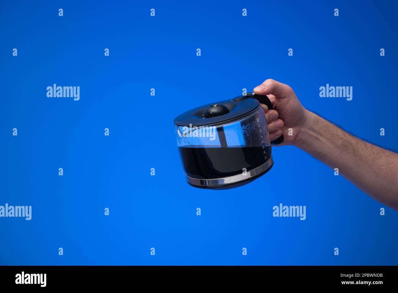 Hausgemachte große Kaffeekanne aus Glas, die ein Mann mit einer Gießgeste in der Hand hält. Nahaufnahme des Studios, isoliert auf blauem Hintergrund. Stockfoto