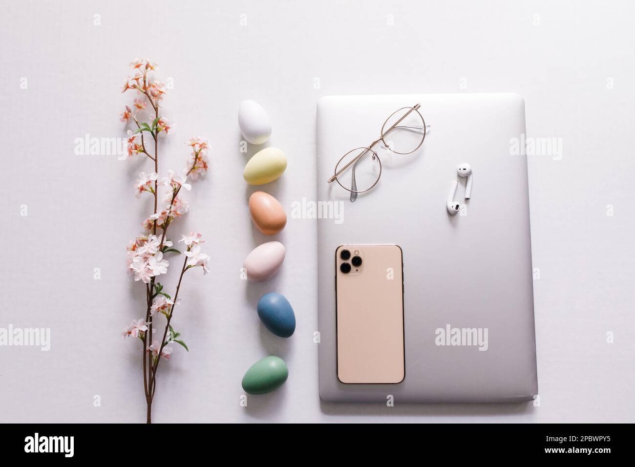 Frühlingsblumen, bunte Eier, geschlossener Laptop, Telefon, Ohrstöpsel Stockfoto