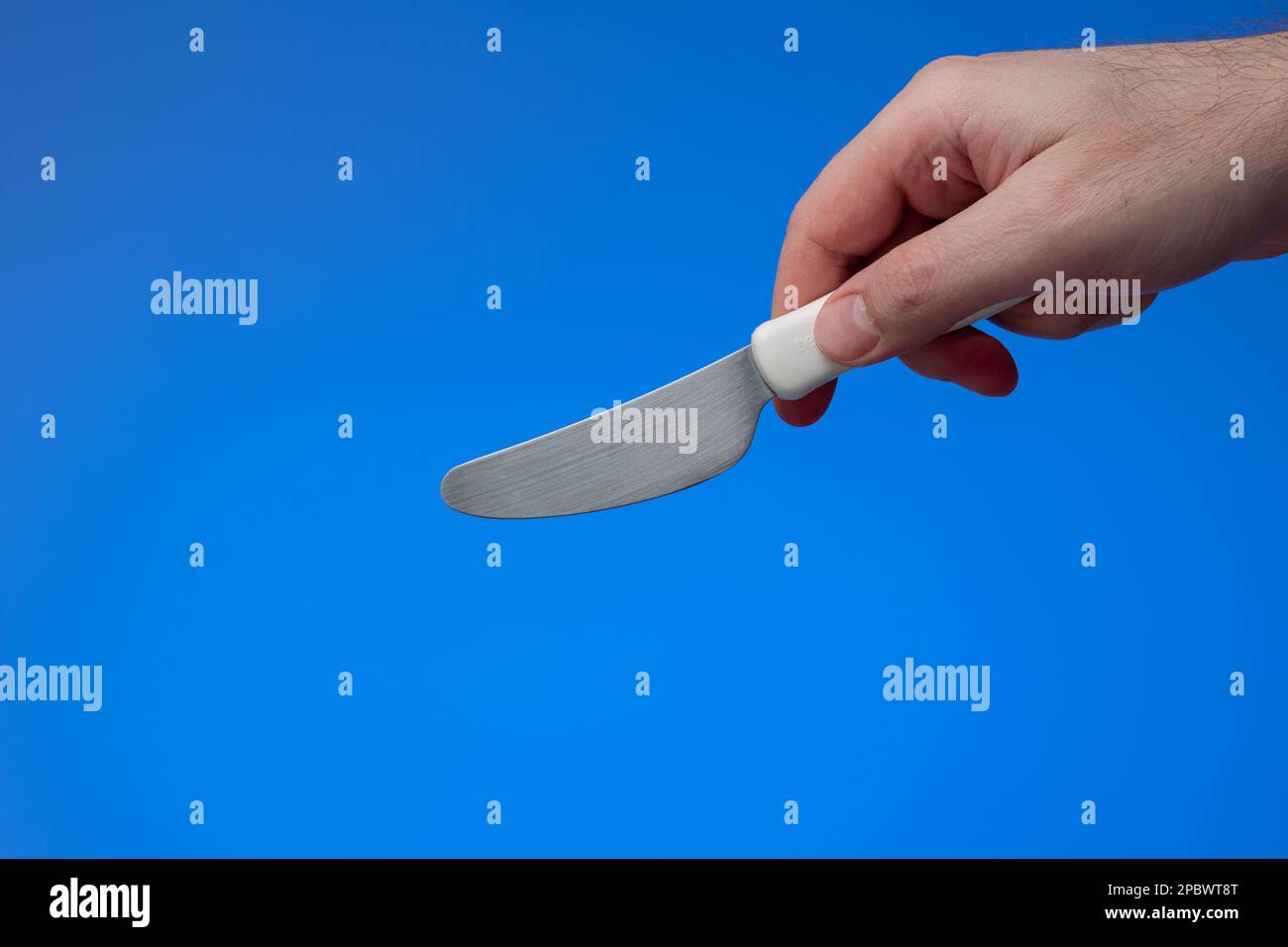 Kleines Küchenmesser mit weißem Kunststoffgriff, der von männlichen Händen gehalten wird. Nahaufnahme des Studios, isoliert auf blauem Hintergrund. Stockfoto