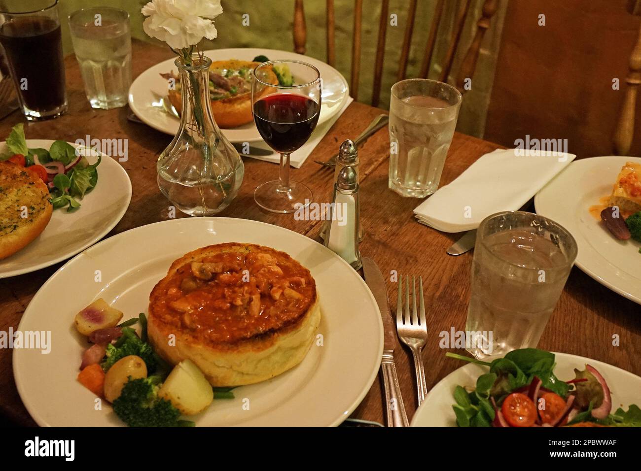 Gebackenes Brötchen und traditionelle britische Gerichte aus nächster Nähe, serviert mit grünem Salat und Rotwein Stockfoto