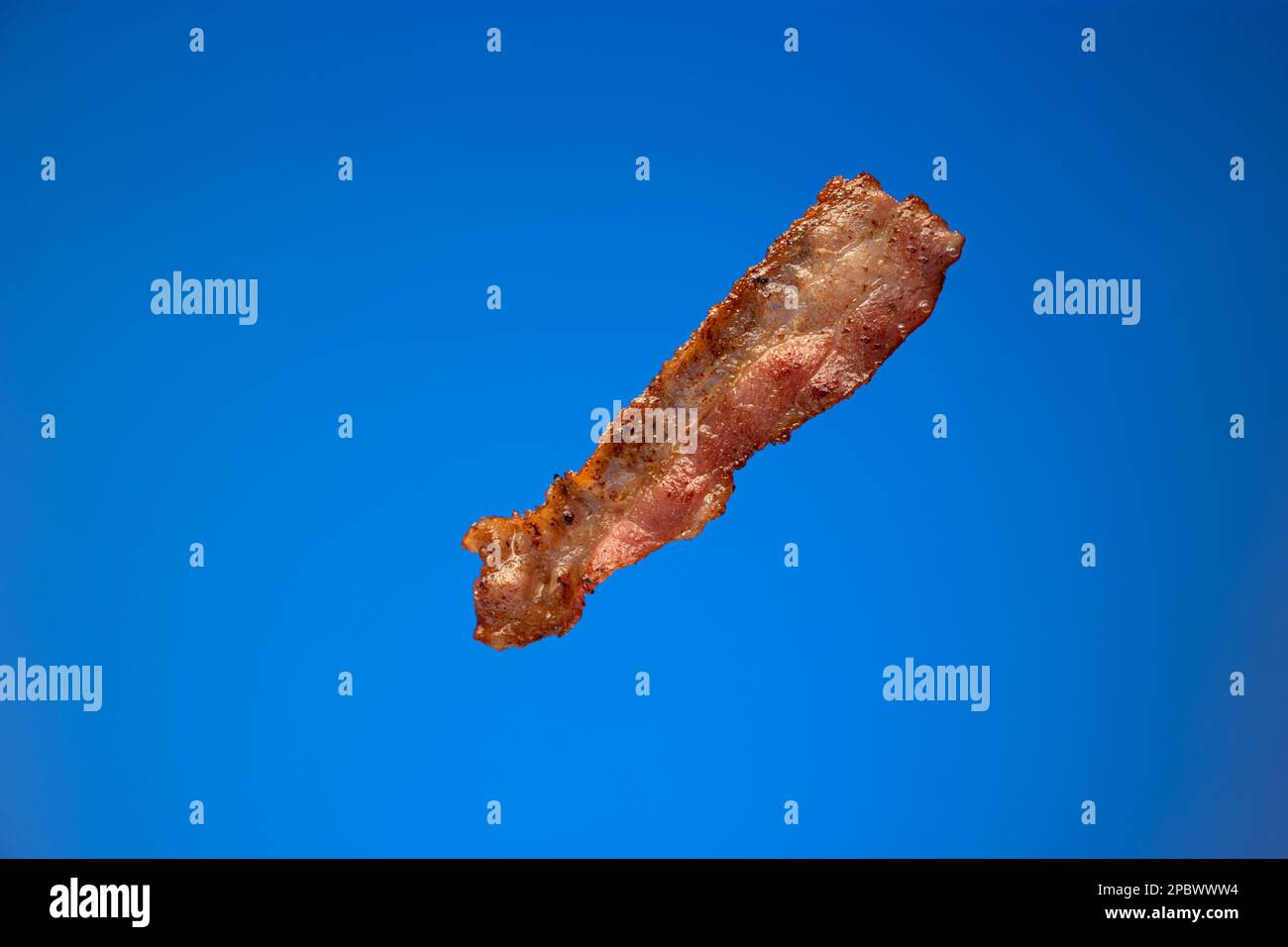 Knusprig gebratener Speckstreifen oder -Scheiben. Nahaufnahme des Studios, isoliert auf blauem Hintergrund... Stockfoto