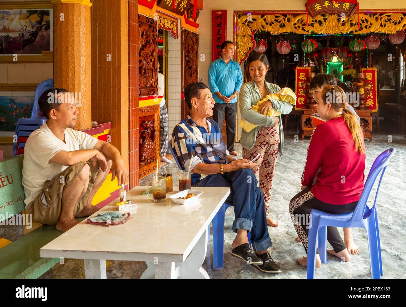 Ein Wahrsager in einem taoistischen Tempel in Tan Chau im vietnamesischen Mekong-Delta spricht mit einer Familie mit einem neugeborenen Baby. Stockfoto