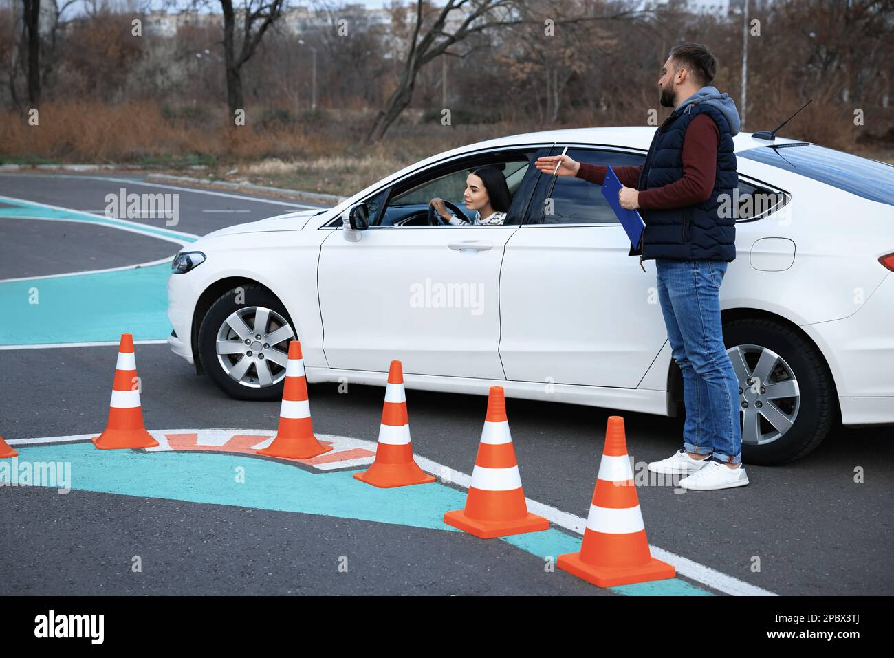 Ausbilder in der Nähe des Fahrzeugs mit seinem Schüler während der Prüfung auf der Fahrschule-Teststrecke Stockfoto